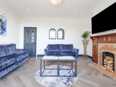 A living room with blue sofas a glass coffee table and a fireplace at Gwynfa in Barmouth