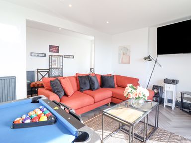 A living room with a red sectional sofa a blue pool table and a glass coffee table with flowers at Gwynfa in Barmouth