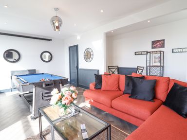 A game room with a pool table a red sectional sofa and a glass coffee table with flowers at Gwynfa in Barmouth