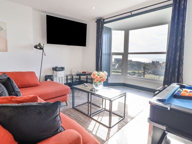 A living room with red sofas a glass coffee table with flowers a pool table and a wall mounted tv at Gwynfa in Barmouth