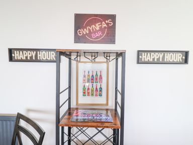 A bar area with a metal and wood frame rack with a gaming room sign and framed bottle artwork on a white wall at Gwynfa in Barmouth