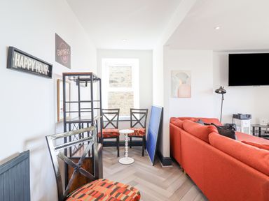 A living room with an orange sofa two chairs with patterned cushions a small white round table and a wall mounted television at Gwynfa in Barmouth