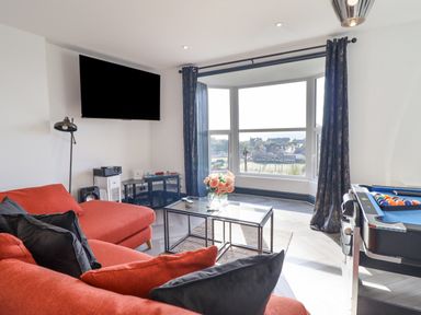 A living room with a red sofa a glass coffee table with flowers a wall mounted tv and a pool table at Gwynfa in Barmouth