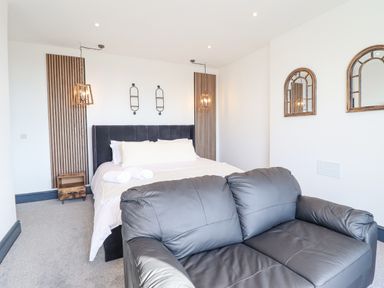A bedroom with a black sofa in front of a bed with white bedding and wooden wall panels at Gwynfa in Barmouth