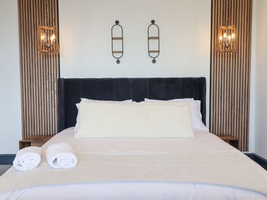 A bed with a black headboard white bedding two rolled towels and pendant lights on wooden panels at Gwynfa in Barmouth