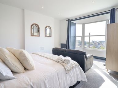 A bedroom with a bed with pillows and towels a black sofa and a large window with curtains at Gwynfa in Barmouth