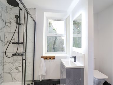 A bathroom with a glass shower enclosure a sink with a mirror and a toilet at Gwynfa in Barmouth