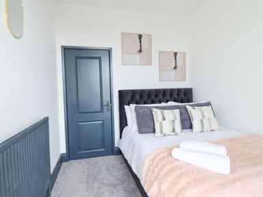 A bedroom with a bed with pillows and a blanket a blue door and radiator and two pictures on the wall at Gwynfa in Barmouth