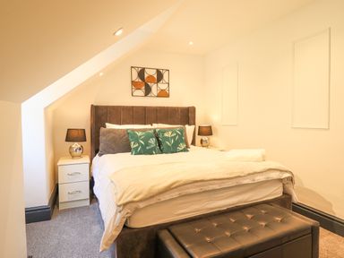 A bedroom with a bed a bedside table with a lamp and a cushioned bench at Gwynfa in Barmouth