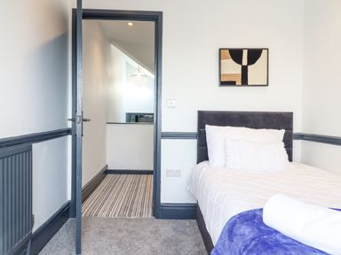 A bedroom with a bed and pillows a door leading to a hallway with a chandelier and striped carpet at Gwynfa in Barmouth