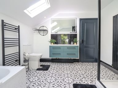 A bathroom with patterned floor tiles a toilet blue vanity with sink and a backlit mirror at Gwynfa in Barmouth
