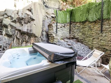 A hot tub with cover and a white lounge chair in an outdoor stone wall area at Gwynfa in Barmouth