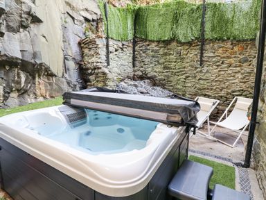 An outdoor hot tub with partially removed cover next to two white deck chairs and stone walls at Gwynfa in Barmouth