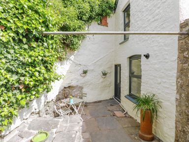 A small outdoor patio with stone flooring a table with two chairs plants on the wall and a potted plant by a white stone house at Suffolk House in Narberth