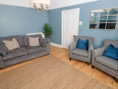 A living room with a grey sofa with beige cushions two striped armchairs with blue cushions and a woven rug at Suffolk House in Narberth