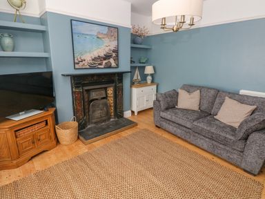 A living room with a gray sofa, a fireplace, a television on a wooden stand, and shelves with decorations at Suffolk House in Narberth