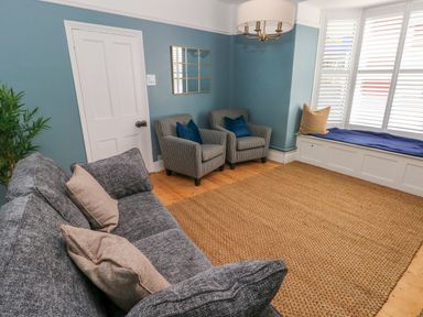 A sitting room with a grey sofa, two armchairs, a wicker rug, and a window seat at Suffolk House in Narberth