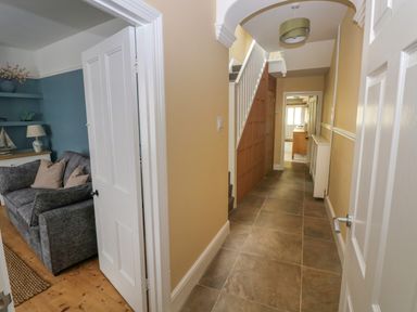 A hallway with tiled floor and staircase next to a room with a gray sofa and blue walls at Suffolk House in Narberth