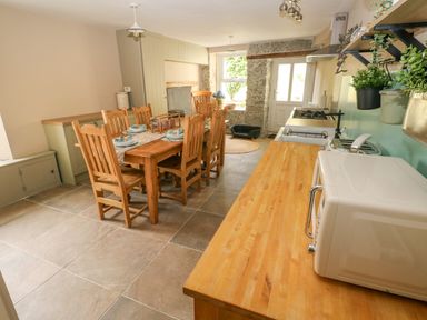 A kitchen and dining area with wooden table and chairs microwave and plants on the counter at Suffolk House in Narberth