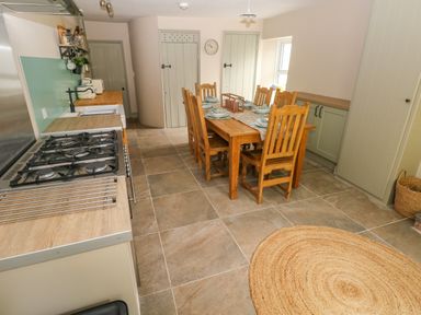 A kitchen with a wooden dining table and chairs a gas stovetop and cabinets at Suffolk House in Narberth