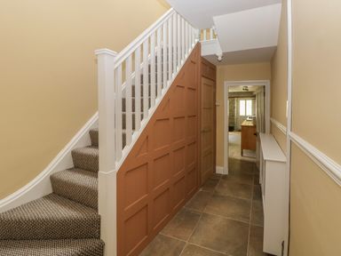 A hallway with tiled floor carpeted stairs and a door under the stairs at Suffolk House in Narberth