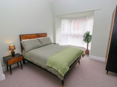 A bedroom with a bed bedside table lamp wardrobe and plant by a window at Suffolk House in Narberth