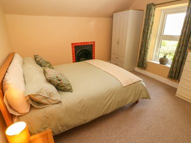 A bedroom with a bed pillows wardrobe window with curtains and a lamp at Suffolk House in Narberth