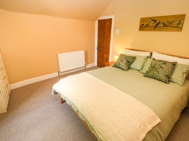A bedroom with a bed with green bedding and floral pillows a wooden door and a dresser at Suffolk House in Narberth