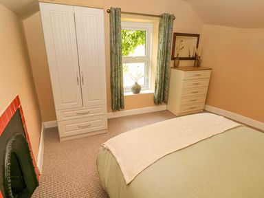 A bedroom with a bed a window with curtains a wardrobe a chest of drawers and a fireplace at Suffolk House in Narberth