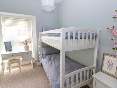 A bedroom with a white bunk bed striped bedding a white desk and chair flower vase and framed artwork at Suffolk House in Narberth