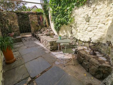 A small outdoor patio with stone flooring green chair and table set and potted plants at Suffolk House in Narberth