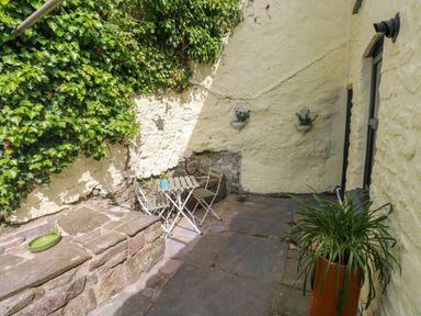 A small outdoor patio area with a stone bench a table with two chairs and climbing ivy on walls at Suffolk House in Narberth