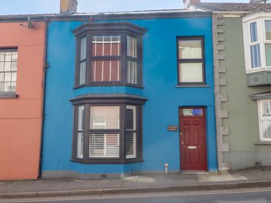 A blue house with red door and bay windows between an orange and a green house at Suffolk House in Narberth