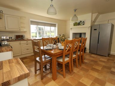 A kitchen with a wooden dining table set for six near a window and a stainless steel fridge at Rempstone Farmhouse Corfe Castle