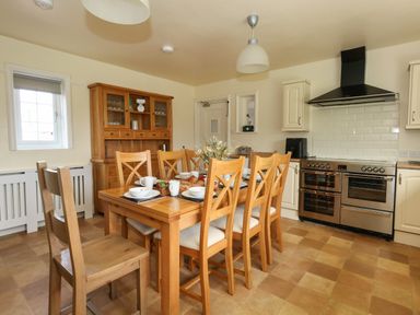 A kitchen with a wooden dining table and chairs set with dishes and food at Rempstone Farmhouse in Corfe Castle