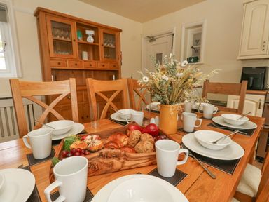 A dining table set with white dishes and mugs with a wooden cabinet in the background at Rempstone Farmhouse in Corfe Castle