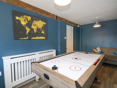 A game room with an air hockey table a brown couch with cushions world map wall art and blue walls at Rempstone Farmhouse in Corfe Castle