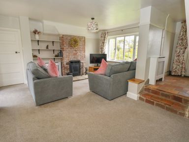 A living room with two sofas facing a brick fireplace and a TV near a window at Rempstone Farmhouse in Corfe Castle