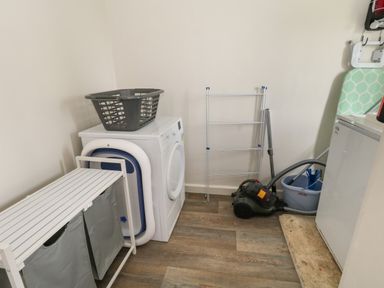 A laundry room with a washing machine a laundry basket a drying rack a vacuum cleaner and an ironing board