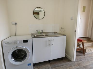 A laundry room with a washing machine a sink cabinet and a round mirror at Rempstone Farmhouse in Corfe Castle