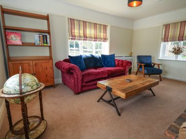 A sitting room with a red sofa blue armchair wooden coffee table and globe at Rempstone Farmhouse in Corfe Castle