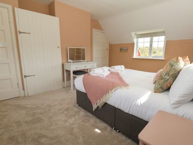 A bedroom with a double bed with pillows and towels a dressing table with a mirror a window and two doors at Rempstone Farmhouse in Corfe Castle