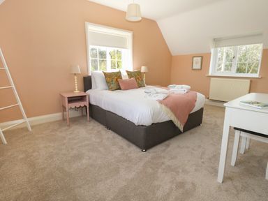 A bedroom with a double bed bedside tables lamps a white desk and chair and two windows at Rempstone Farmhouse in Corfe Castle