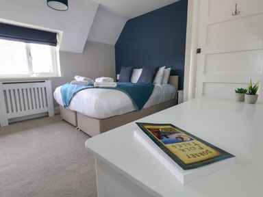 A bedroom with a bed with towels on it a book on a white table and a window with a blue blind at Rempstone Farmhouse in Corfe Castle