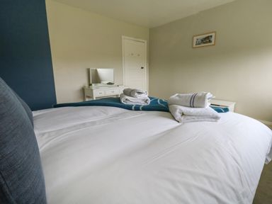 A bedroom with a bed with folded towels on it a white dresser a mirror and a framed picture on the wall at Rempstone Farmhouse in Corfe Castle