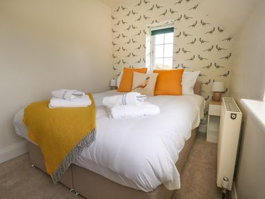A bedroom with a bed with orange cushions and folded towels on top at Rempstone Farmhouse in Corfe Castle