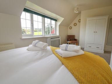 A bedroom with a bed covered with white sheets and a yellow blanket with folded towels on top and a window with green scenery outside at Rempstone Farmhouse in Corfe Castle