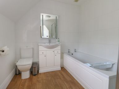 A bathroom with a toilet sink with a mirror and a bathtub with taps at Rempstone Farmhouse in Corfe Castle