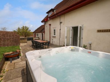 An outdoor patio area with a hot tub table and chairs near a beige building at Rempstone Farmhouse in Corfe Castle