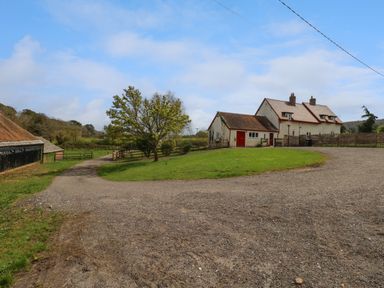 A farmhouse with red doors next to a gravel driveway and trees at Rempstone Farmhouse in Corfe Castle